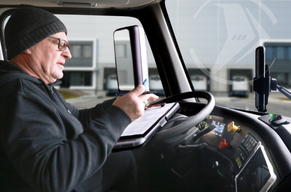 Truck driver filling out paperwork inside the cab of a commercial vehicle at a distribution center.
