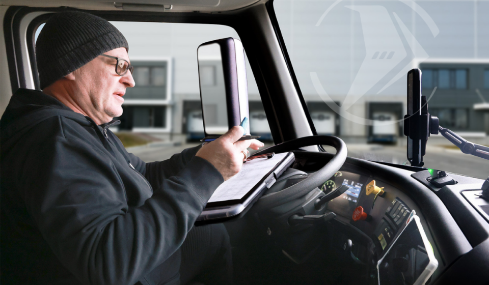 Truck driver filling out paperwork inside the cab of a commercial vehicle at a distribution center.